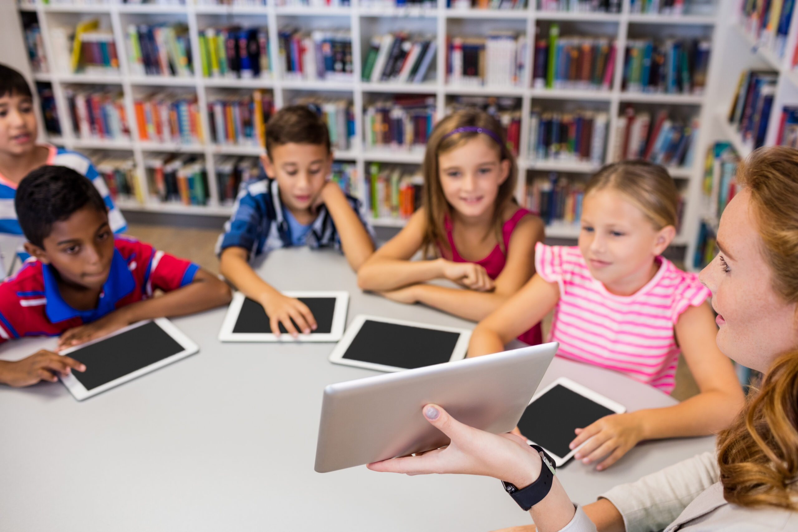Young pretty teacher having lesson to children with their tablet at school